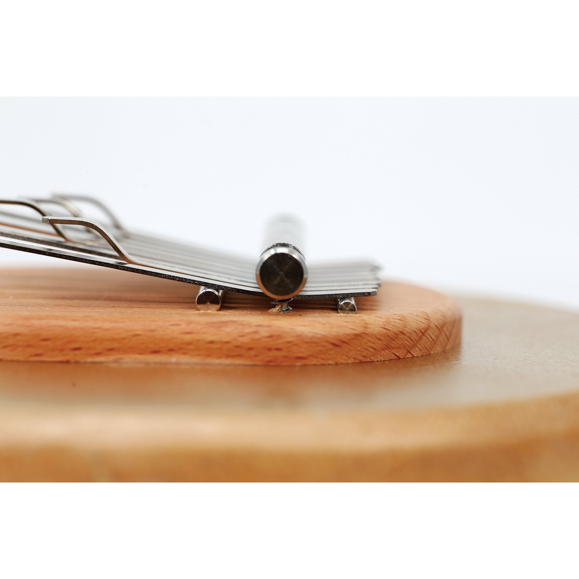 Side close-up of kalimba tines and wooden bridge on clear skin bowl, focusing on metal tines