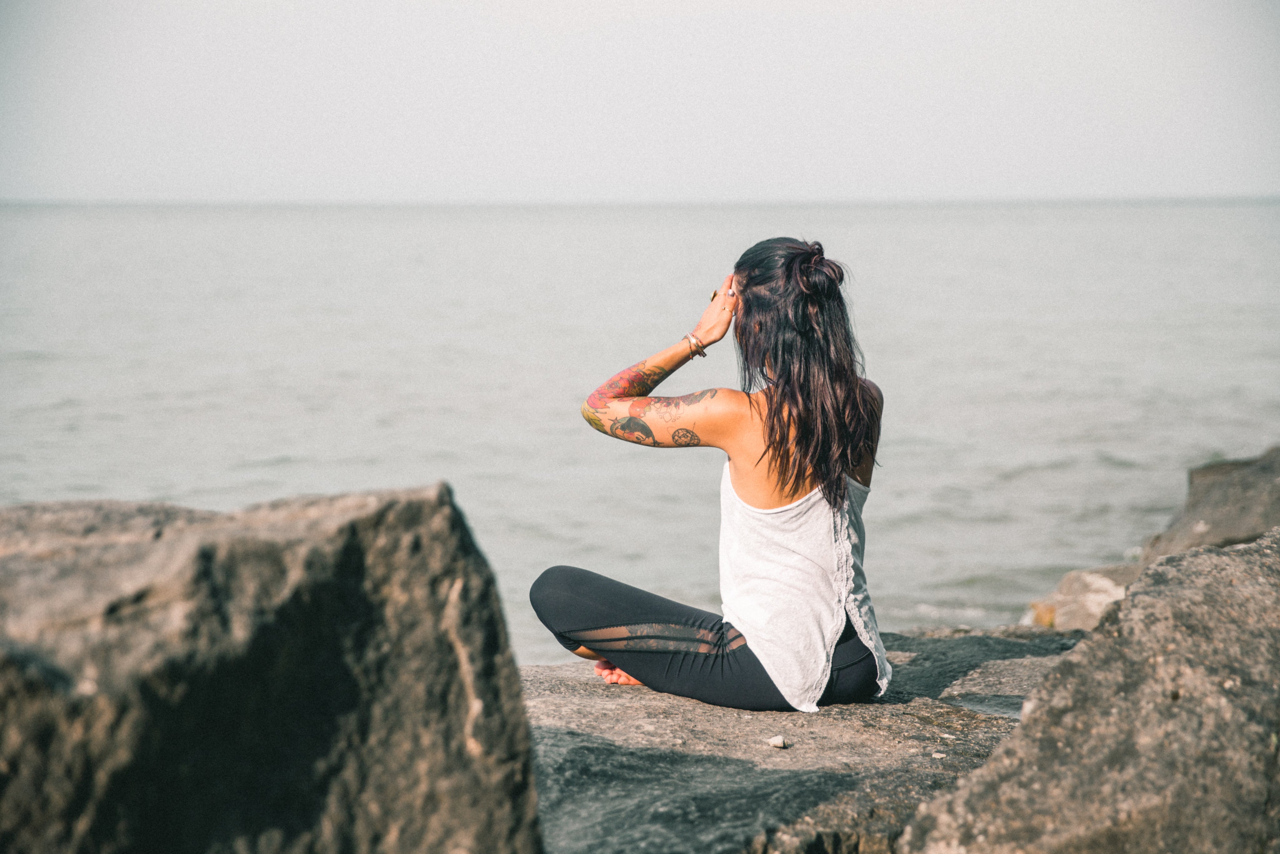 Woman meditating outdoors on a yoga mat near the ocean representing calm and balance.