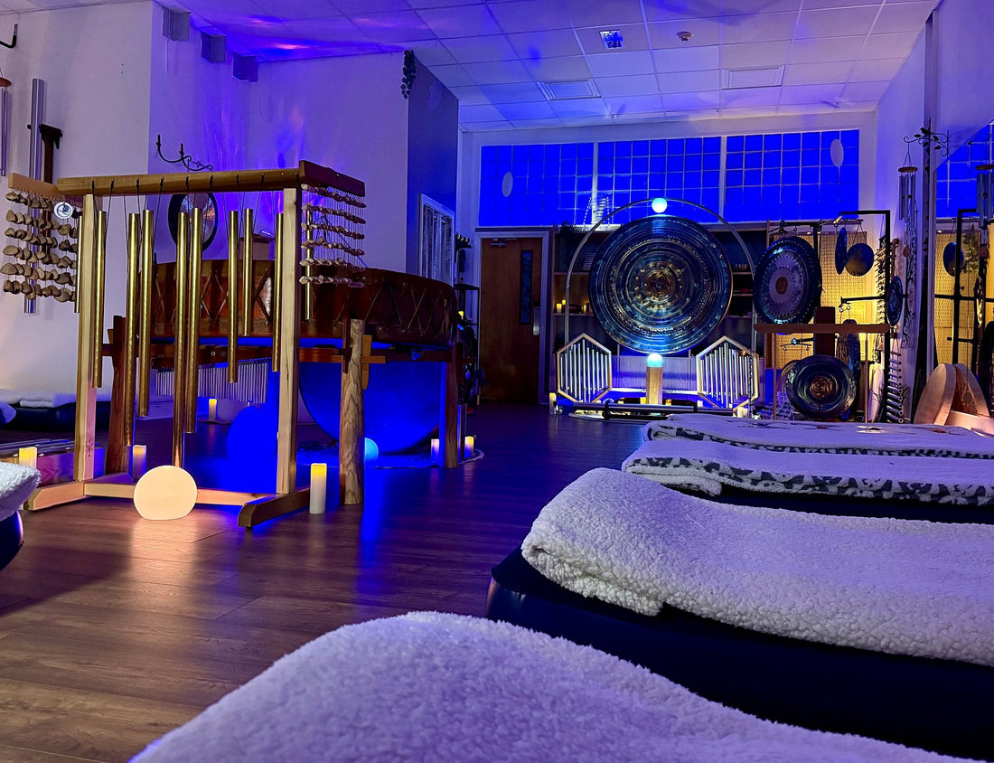 Air beds with blankets set out in the Revival Harmony studio under soft blue light, with chimes and a gong at the front