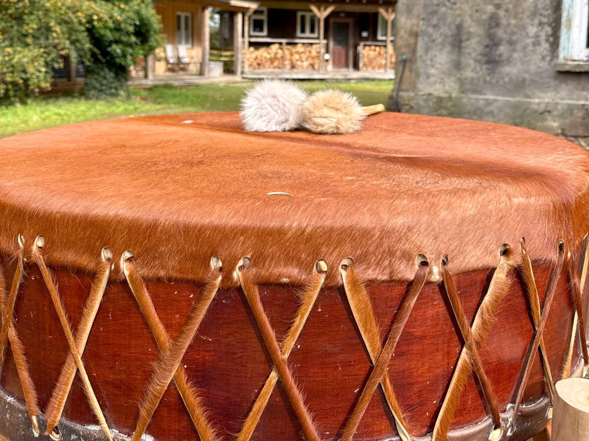 Close up of a laced hide drum with two beaters, cabins behind